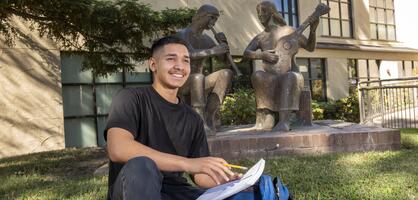 Student sitting on grass with notebook smiling