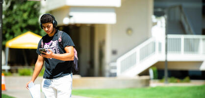 Photo of a student walking through Dolores Huerta Plaza looking at his phone