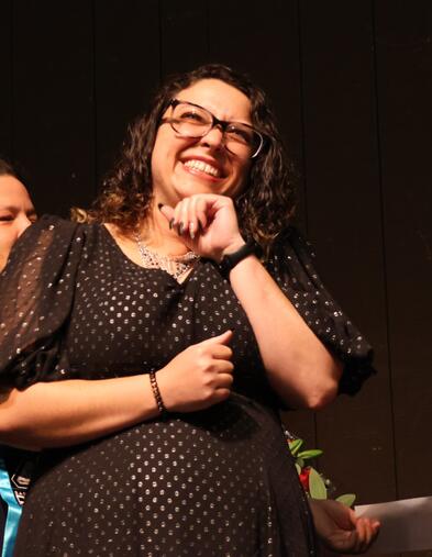 Student standing on stage smiling out at audience