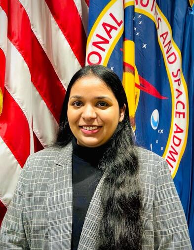 Portrait of student smiling wearing blazer in front of two flags
