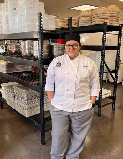 Culinary student wearing chef attire standing and smiling in front of culinary tools