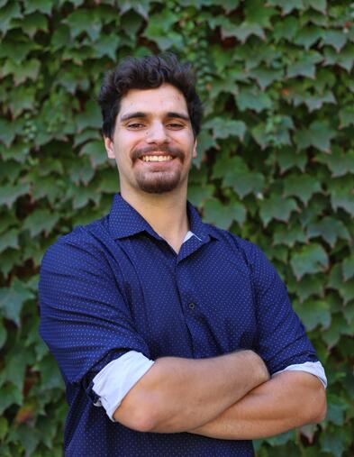 Student smiling and standing with arms crossed in front of ivy