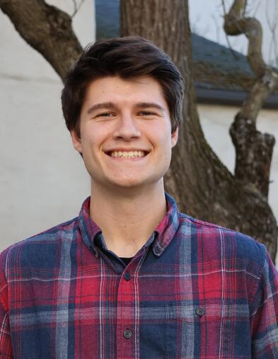 Portrait of student smiling and standing in front of a tree and building