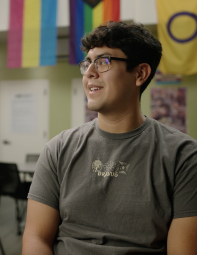 Student sitting in Pride Center room with Pride flags behind them