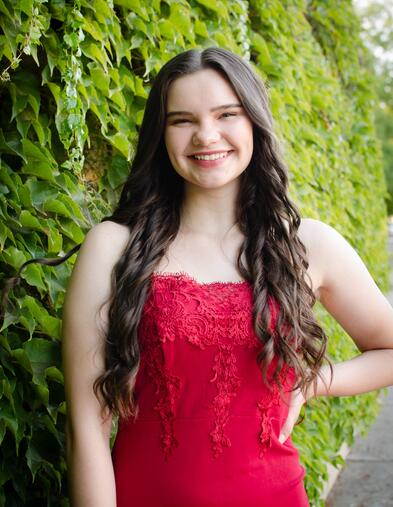 Student wearing red dress smiling in front of ivy