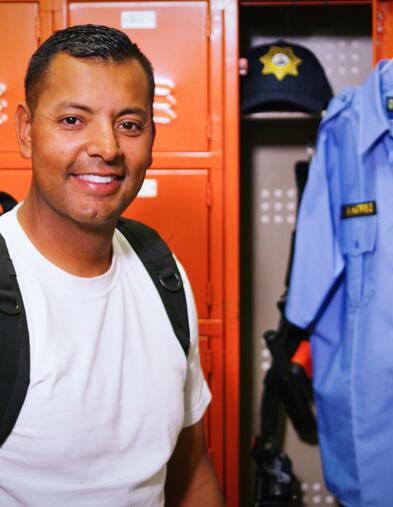 POST Academy student standing and smiling in front of orange lockers and POST uniform