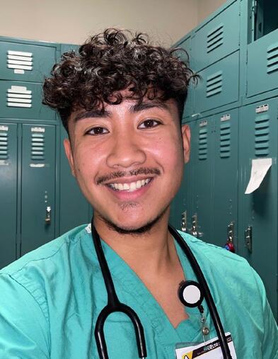 Selfie of student wearing nursing scrubs smiling with lockers behind them